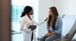 Stock image of a doctor speaking with a teenage girl in a doctor's office exam room