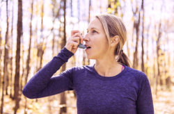 Stock photo of a woman runner outside using her inhaler to breathe