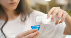 Stock photo of a woman pouring eye wash liquid into the glass to soothe and cleanse eyes.