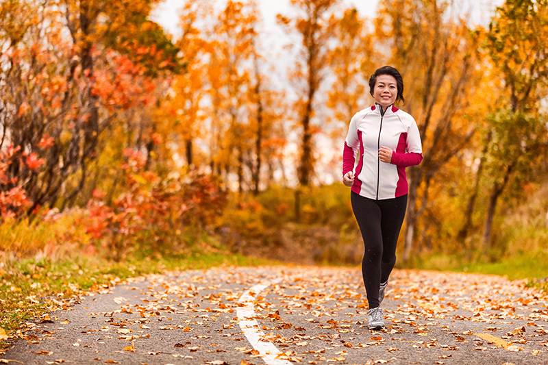 Middle age active lifestyle Asian woman living a healthy life running in park path autumn forest.