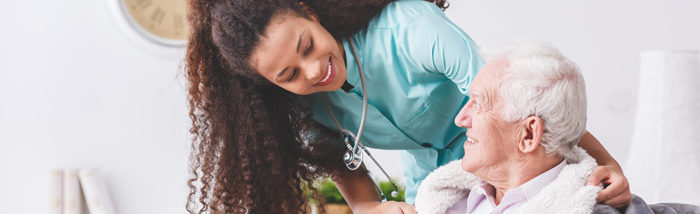 Panorama of a happy nurse with a stethoscope covering an elderly man with a blanket in a nursing home